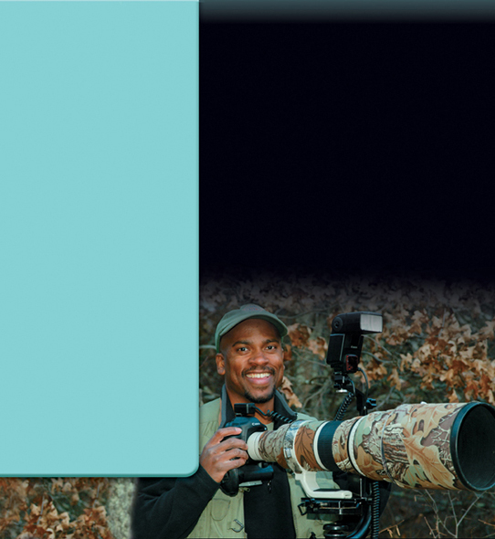 A photograph of Dudley Edmondson, a wildlife photographer shown standing with a photography camera. 