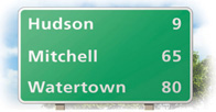 A sign shows 9 miles until Hudson, 65 miles until Mitchell, and 80 miles until Watertown.