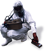 A scientist in protective gear uses handheld machinery.