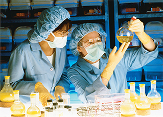 Two scientists wear protective gear as they work with chemicals in a lab. 