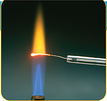 Closeup of two flames. Bottom flame is blue; top flame is orange. The top flame is held over the bottom flame with a wire loop. 