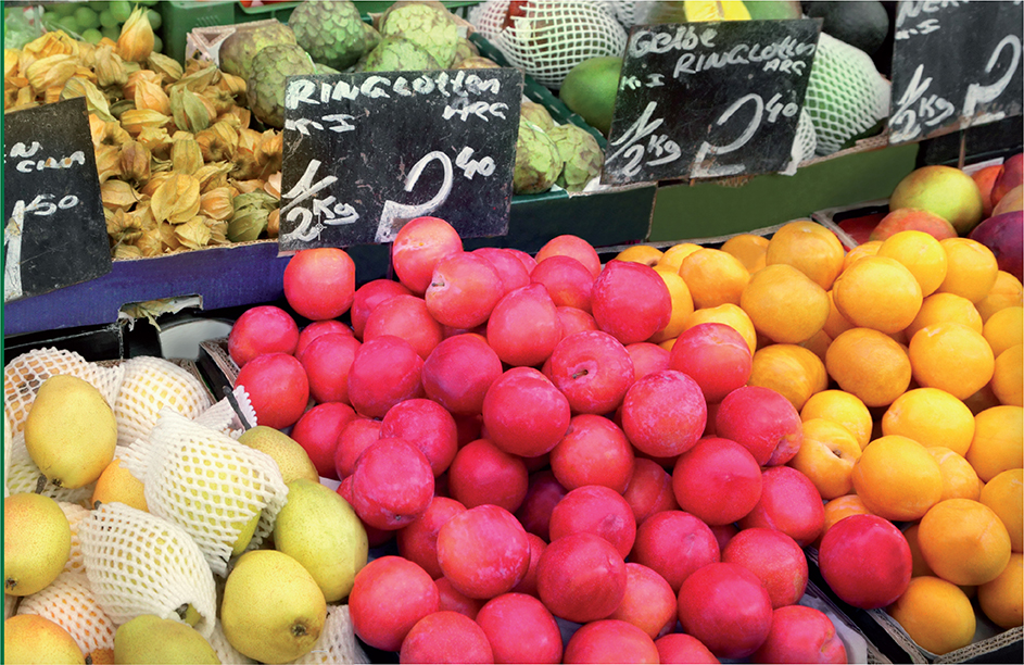 Fruits and vegetables arranged and labeled in a stall for sale.