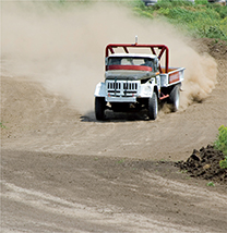 A jeep is driven on a secluded dirt road, kicking up a cloud of dust.