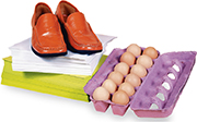 A pair of shoes on top of a pile of paper, next to a carton of one dozen eggs.