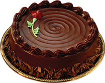 A round chocolate cake with a flower on the side and chocolate shavings at the bottom.