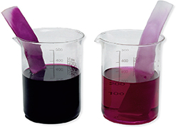Two beakers filled halfway with different colored dye solutions. Each contains a fabric strip sticking out of the beaker.