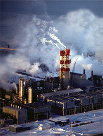 An aerial view of an industrial plant. The towers of the plant emit smoke into the air.