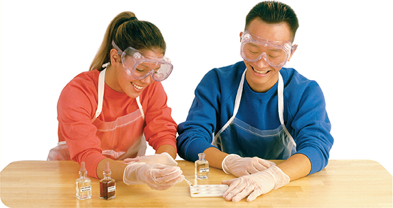 Two students perform a lab experiment. The female student uses a dropper to put liquid into a tray. The male student watches and holds the tray in place. 