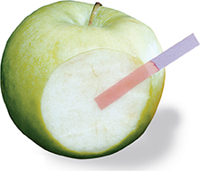 A Granny Smith apple with a bite taken out of it. A strip of blue litmus paper touching the inside of the fruit turns pink.