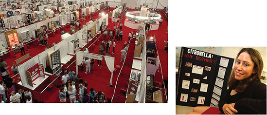 A science fair. There are aisles of booths with  scientific displays and people walking around from booth to booth. A smaller image is shown to the right, which is a closeup of a woman at her science fair booth.