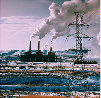 A coal burning power station in snowy terrain, blowing thick clouds of smoke into the air.