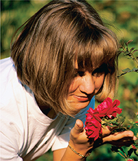A woman smells a flower growing outside.