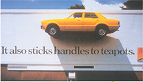 A billboard with a car glued to the side of the billboard. The words "It also sticks handles to teapots" is on the billboard beneath the car, as a means of advertising for adhesive.