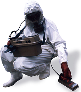 A scientist in protective gear uses handheld machinery.