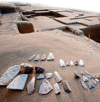 Photo of old stones that are in the shape of jagged tools or weapons lying on sandy ground.