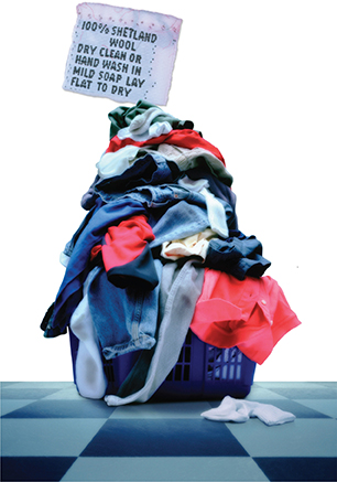 A pile of dirty laundry on a hamper.  A large label on the pile says 100% shetland woll, dry clean or hand wash in mild soap, lay flat to dry.
