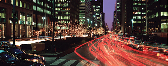 A busy city with tall buildings and traffic in motion, creating a blur of lights in the street.