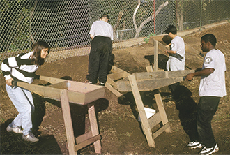 Photo of students sifting through wooden screens containing dirt. 