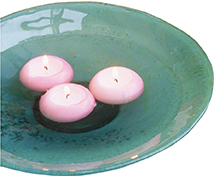 Three small lighted candles float in a dish of water.