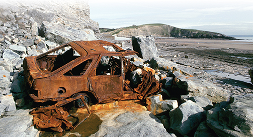 Photo of a rusty old automobile set upon  rocks.
