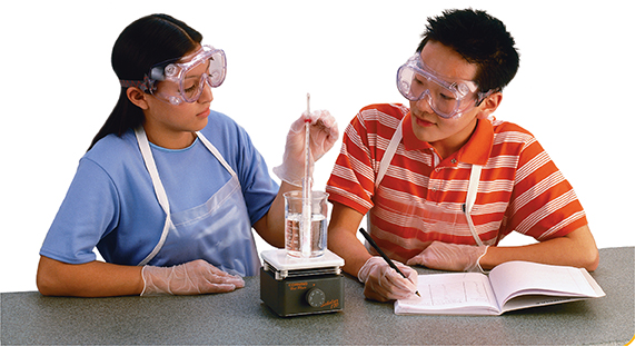 Photo of two students in a lab performing an experiment. The female student holds the thermometer sticking out of a beaker placed on a burner. The male student sits next to her taking notes in a notebook.