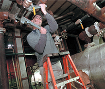 A heating and cooling technician working with pipes in the ceiling. 
