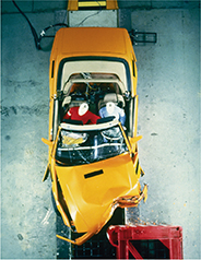 Photo of an aerial view of a test car colliding with test dummies in the vehicle, showing the force of the collision.