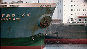 The hull of a large steel ship. The ship floats in the water at the dock.
