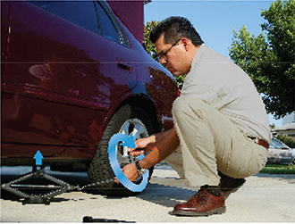 A man squatting low to change a tire. He is turning the jack handle in a circular motion to help lift the car off the ground. 