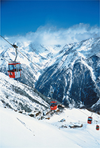 Cable cars move along a cable over snow capped mountains.