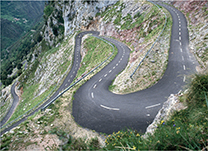 An aerial view of a long and winding road.  The road is on an incline, going up a mountainside.  