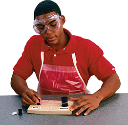 A male student at a desk wearing safety goggles, working with his lab model per the instructions in this exercise.