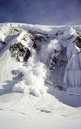 An avalanche takes place on snow covered mountains.  