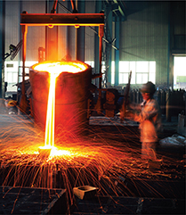 A worker in a factory stands beside a large vat of molten metal. The vat is slightly tilted and molten metal  pours out, emitting bright light. 