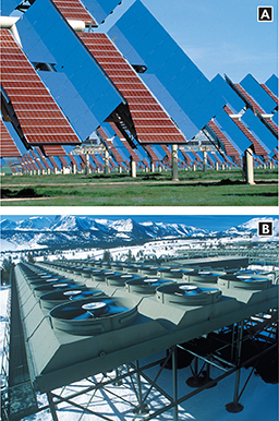 Buildings with large  solar panels on its sides, and a rows of wind turbines.