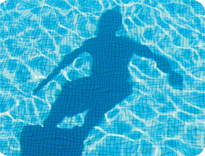 A pool of water with bright gridlines on the bottom, with the silhouette of a person on a diving board.

