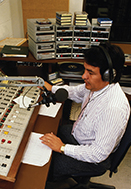 A radio announcer working in front of a sound board.