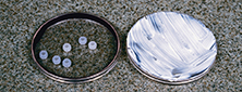 Two petri dish lids, one with sun screen spread onto it, the other with six ultraviolet-detecting beads.  You will evaluate sun screen in this lab.