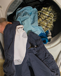 Clothes being removed from a dryer with a sock sticking to a pair of pants.