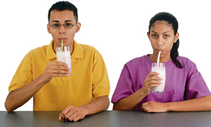 A boy and girl drinking a beverage using straws of different thickness. 