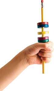 A hand holding a pencil with five circular magnets. Two magnets are stuck together, one magnet is in the middle alone and another two magnets are stuck together below it. 