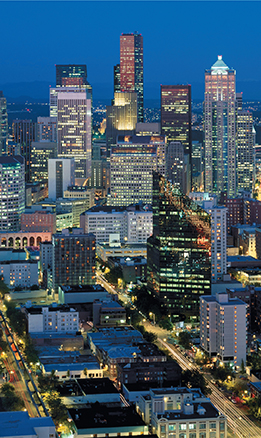 A cityscape of Seattle, Washington.  The lights are on in most of the buildings and also on the streets.