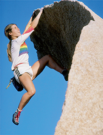 A female rock climber hanging on to the edge of a rock.  She is not using a rope or harness.