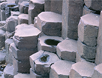 Hexagonal columns of basalt.  These hexagonal boulders are stacked on top of one another.  Two are shown with a hole in the middle.