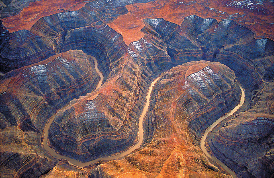 An aerial view of canyons of sedimentary rock with a river winding through it.