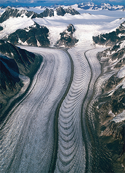 A glacier begins near a mountain peak and winds down through a valley. The valley portion has ripple marks.