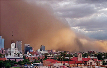 A dust storm looming over a city.  The dust has formed a large cloud above the city. Buildings and homes are in the city.