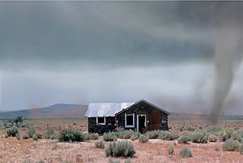 A tornado over a farm field, with a small farmhouse in its path.