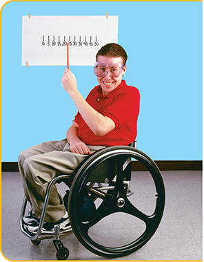 A male student in a wheel chair pointing to a measurement scale on a wall.