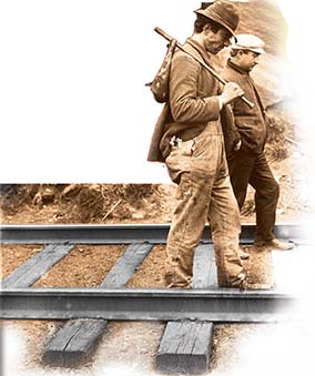 Two homeless men walk along railroad tracks.